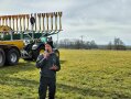 Mann mit einem Mikrofon steht vor einer großen Maschine mit Anbau zur Gülleausbringung