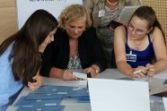 3 Personen sitzen an einem Tisch und schauen auf Spielkarten