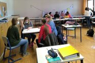 Personen sitzen an Tischen in Klassenzimmer