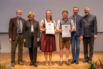 6 Personen stehen nebeneinander, 2 davon halten Urkunden