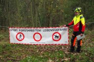 Forstwirt vor einem Absperrbanner mit Text: Stopp! Forstarbeiten! Lebensgefahr