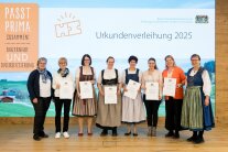 8 Personen stehen nebeneinander und halten Urkunden