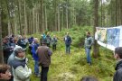 Teilnehmer am Waldbegang stehen im Kreis um Referent vor einem Plakat