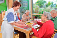 Frau reicht Seniorin Teller mit Essen